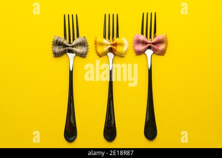 three forks with pieces of pasta with the shape of a colored butterfly on a yellow surface Stock Photo