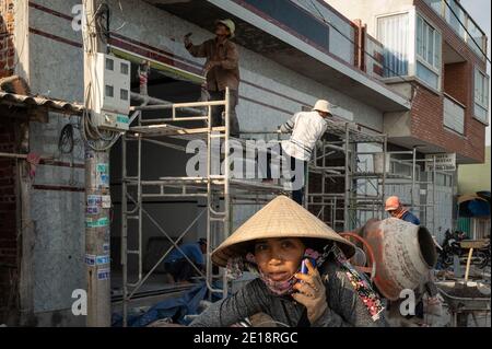 Woman on her phone with construction workers in the background, Phuoc Hai, Vietnam Stock Photo