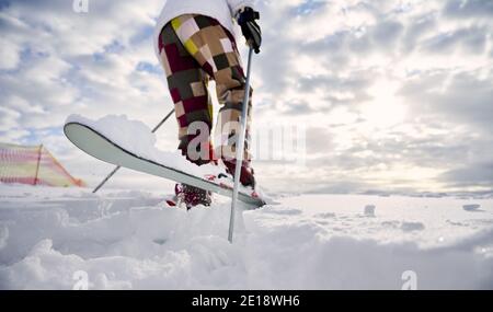 Close-up, low angle view snapshot of skier's legs. Man skiing, making a jump up on white snowy surface against beautiful cloudy sky. Copy space. Concept of winter sport activities.