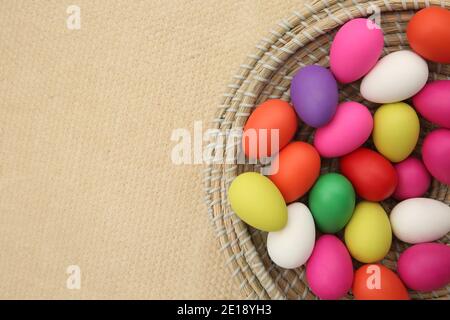 Brightly colored easter eggs, in a straw basket against a beige background.