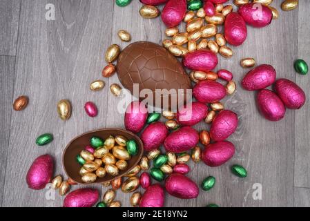Pile or group of multi colored and different sizes of colourful foil wrapped chocolate easter eggs in pink, red, gold and green. Large halves of a bro Stock Photo