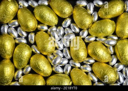 Large & small yellow, gold and silver foil wrapped chocolate easter eggs, against a black background. Stock Photo