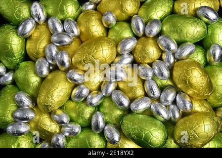 Large & small yellow, gold, green, lime green and silver spring colours of foil wrapped chocolate easter eggs, against a black background. Stock Photo