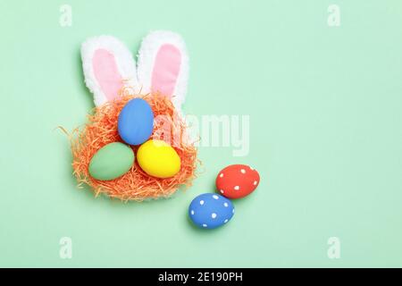 Easter eggs in a nest, bunny ears on a mint green background. Greeting card with copy space flat lay. Stock Photo