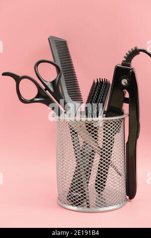 hair stylist tools in a basket. scissors, brush, comb, curling iron, vertical size. pink background. home hair care. beauty salon tools. hairdresser's Stock Photo