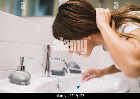 Cute brunette washing mouth with water after brushing her teeth. Stock Photo