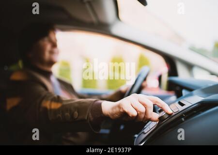 Close up focus view of woman hand turning volume up while driving a car through the city. Stock Photo