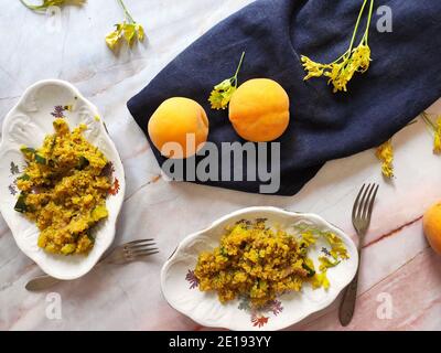 Two oval plates of yellow quinoa with courgettes and peaches Stock Photo
