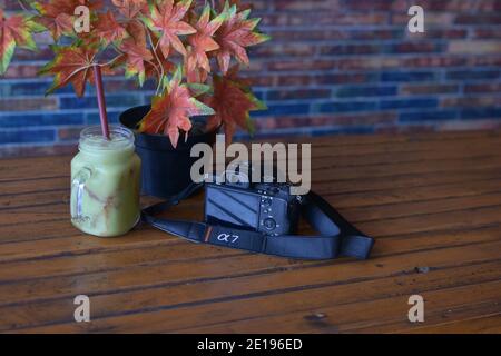 indonesia, 11-23-2020, sony a7 camera and nokia smartphone on a wooden table with a glass of fruit juice and red maple flowers in a pot, this photo ca Stock Photo