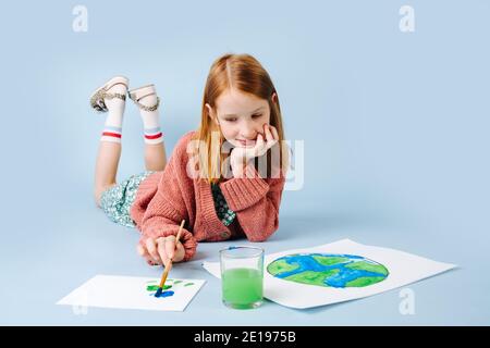 Red-haired girl lying on the floor draws a green-blue planet Stock Photo