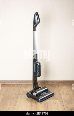 Handheld vacuum cleaner with small dust tank in an empty room. cordless vertical vacuum cleaners without dust bag with cyclone filter. wooden laminate Stock Photo