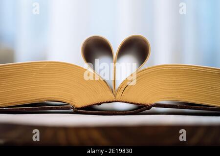 Old opened hardback book  with heart form sheets isolated on a wooden background. Love reading. Close up Heart from book, Vintage color tone. Stock Photo