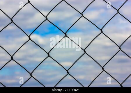 Metal protective grid or netting against a background of blue sky with white clouds. Protected facility, parking lot or prison Stock Photo