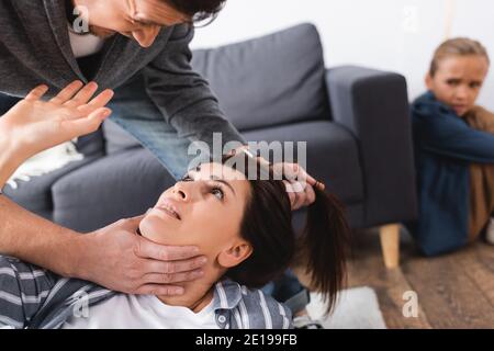 Abusive man holding hair of scared wife near daughter on blurred background at home Stock Photo