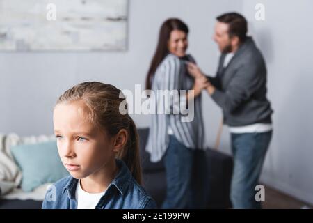 Upset kid standing near parents quarreling on blurred background at home Stock Photo