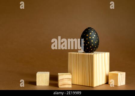 Trendy easter background. Golden and black painted eggs stand on wooden cubes, podiums on brown background Stock Photo