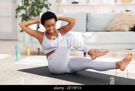 Young black woman exercising in her house gym, doing abs exercises, working out at home during coronavirus quarantine Stock Photo