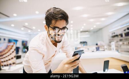 Close up of handsome young man buying new mobile in the electronic shop. Stock Photo