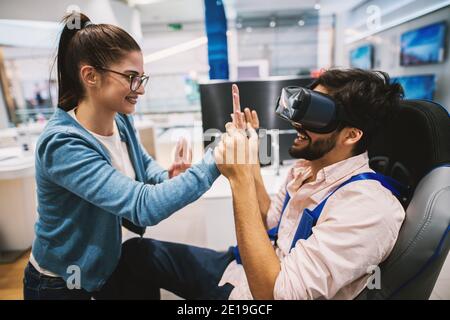 Joyful attractive modern couple having fun testing VR in the electronic store. Stock Photo