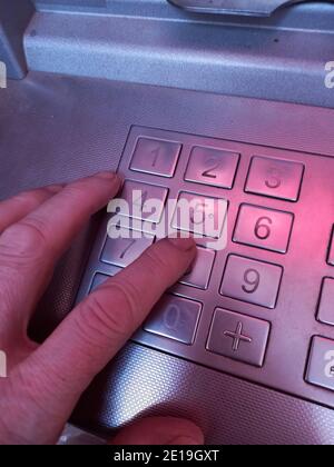 Hand dials pin code on ATM keyboard. Close-up of the left hand of an adult man. Toned photo. Selective focus. Stock Photo