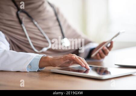Cropped of female doctor with smartphone using digital tablet Stock Photo