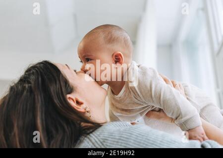 Young mother kissing her cute baby boy on hands in bright room, love emotion Stock Photo
