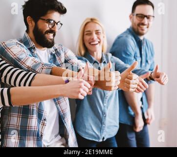 Group of joyful excited young people holding thumbs up while waiting or having a break. Happy team and coworkers concept. Stock Photo