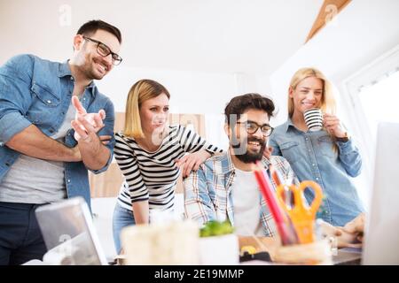 Group of four young satisfied successful business people looking at the final product on a laptop in the office together with pleasure. Stock Photo