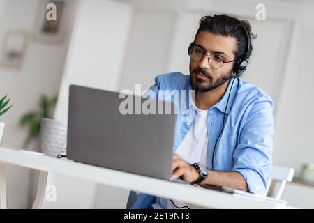 Young Arab Male Hotline Operator In Headset Working With Laptop In Office Stock Photo