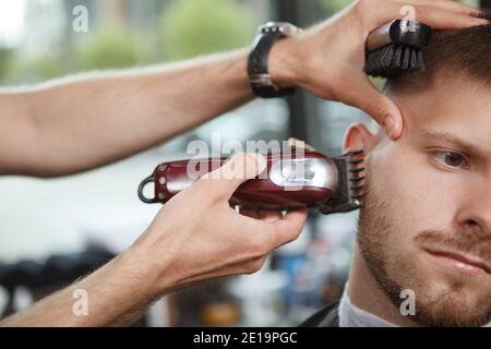 Cropped close up of unrecognizable barber using electric clipper, shaving beard of male client Stock Photo