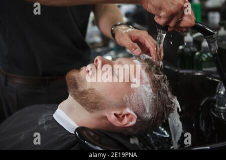 Close up of a barber washing hair of male client, using shampoo Stock Photo