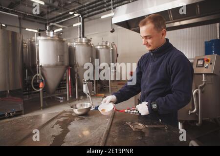 Cheerful young male brewer enjoying working at beer factory, copy space Stock Photo
