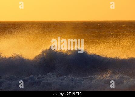Surf at the coast of Cape Town in South Africa with view from the beach on the sea with breaking waves during golden hour before sunset Stock Photo