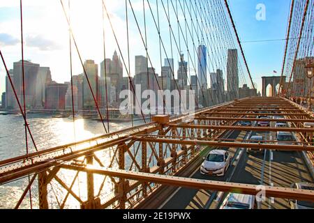 Golden Hour on Brooklyn Bridge in New York City with View on East river and skyline of Manhattan Financial District with car traffic and sun on water