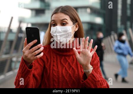 Happy young woman with surgical mask video calling when walking in city street Stock Photo