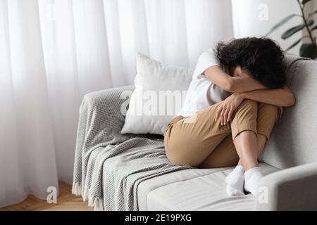 Depressed brunette woman sitting on couch alone, crying Stock Photo