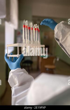 Close up of a hands of a medic in blue rubber disposable gloves holding stand with test tubes system for diagnosis of coronavirus disease. City Stock Photo