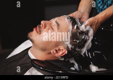 CLose up of a mature man enjoying head massage at the barbershop. Professional barber massaging head of a customer while washing his hair with shampoo Stock Photo