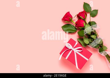 Bouquet of three red roses and gift box on pink background. Birthday, Mother's, women's or Valentine's day greeting. Love and dating concept. Flat lay Stock Photo