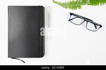 black notebook, pen and glasses on white table background with copy space Stock Photo