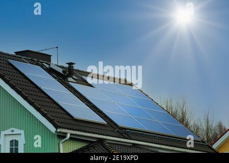 Solar panels on rooftop of a residential suburban house with the Sun shining on clear blue sky. Stock Photo