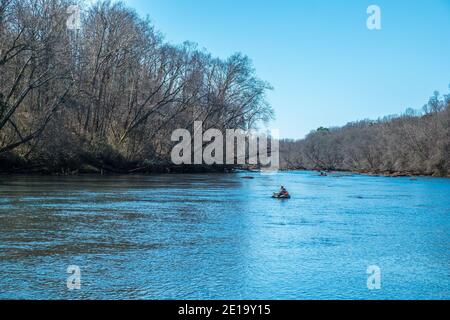 A man fly fishing in a rubber float tube with other people fishing in the distance on the Chattahoochee river going downstream on a bright sunny day i Stock Photo