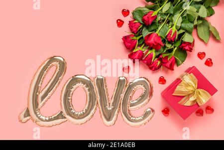 Love word shaped with shiny foil balloon, red roses bouquet, gift box and hearts on pink background. Mother's, women's or Valentine's day Stock Photo