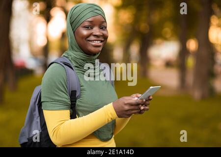 Outdoor Portrait Of Happy Black Muslim Female Student With Smartphone And Backpack Stock Photo