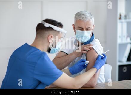 Young doctor making coronavirus vaccine injection to senior male patient at hospital Stock Photo