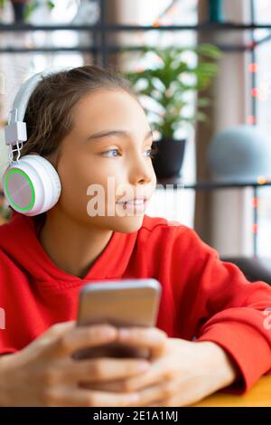 Teenager girl listening to the music via headphones and online app in mobile phone. Modern technology concept. Stock Photo