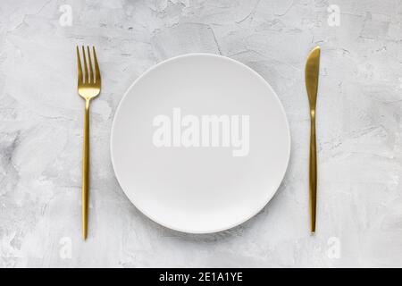 Golden cutlery and empty plate on gray background Stock Photo
