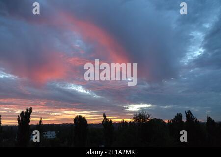 Beautiful painted clouds in the sky before sunrise. Silhouettes of trees against the background of a multi-colored sky during the sunrise. Stock Photo