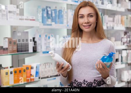 Happy beautiful woman smiling to the camera joyfully, holding products she is buying at the drugstore. Cheerful female customer posing at the pharmacy Stock Photo