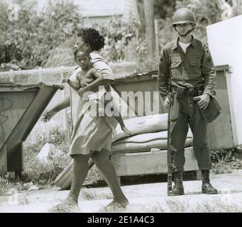 1968 Liberty City Riots.  The Florida National Guard was called out to help quell the violence.  Here a woman carries her child past a National Guardsman.  Miami, Florida. Stock Photo